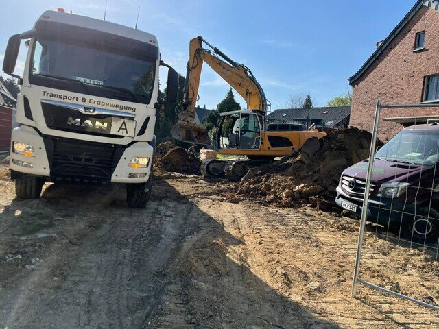 Kettenbagger und Lkw bei Erdarbeiten neben einem Wohnhaus